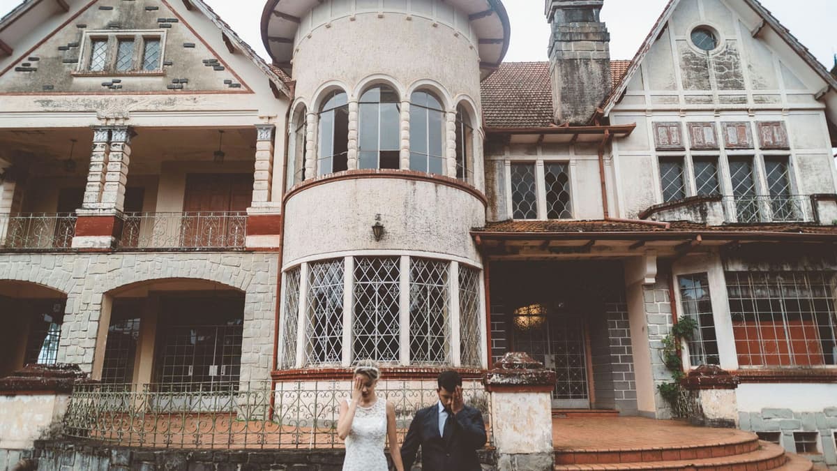 A newlywed couple poses romantically in front of a picturesque historic mansion.
