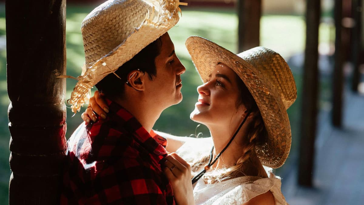 A romantic couple embracing outdoors wearing straw hats, bathed in warm sunlight.