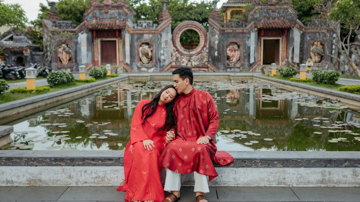 Couple embracing by a lotus pond in traditional Vietnamese attire at a temple in Đà Nẵng, Vietnam.