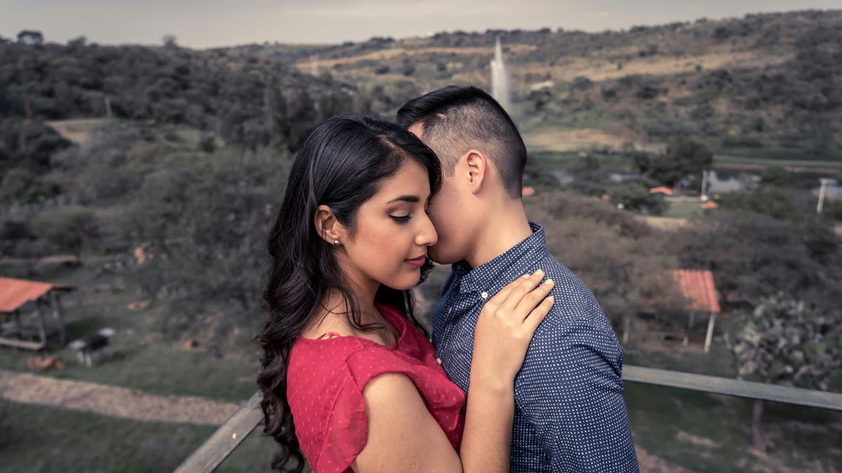 A loving couple embraces on a balcony with scenic rural views.
