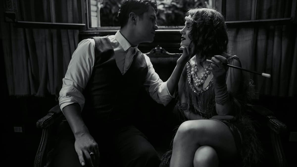 Stylized black and white photo of a fashionable couple in vintage attire sharing an intimate moment indoors.