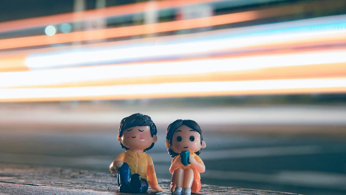 Cute figurines of boy and girl placed near asphalt road with long exposure light trails on street in evening time