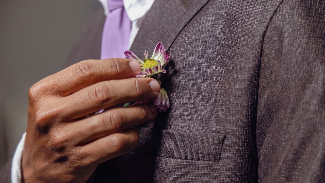 Close-up of a groom adjusting his flower boutonniere, symbolizing wedding elegance.