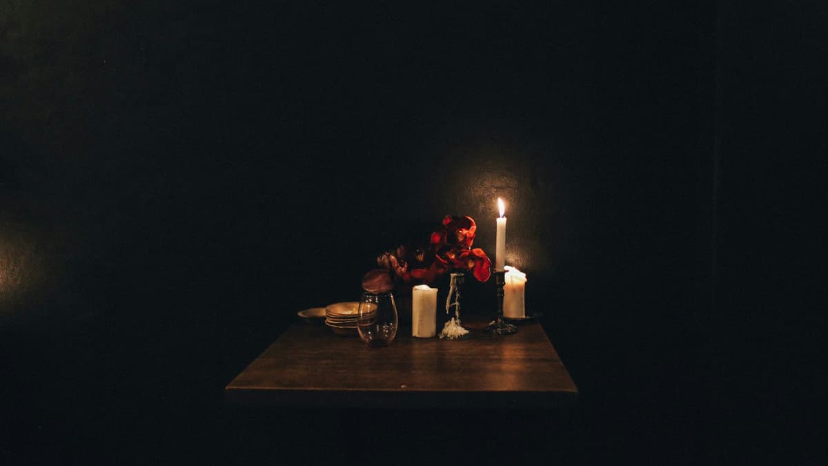 Intimate table setting with candles and red roses at night in a dark room.