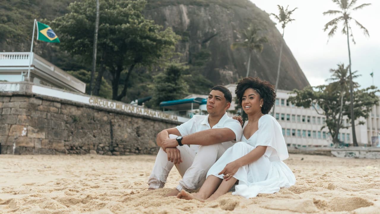 Couple sitting on Copacabana Beach, Brazil, with lush scenery and iconic rock in the background.